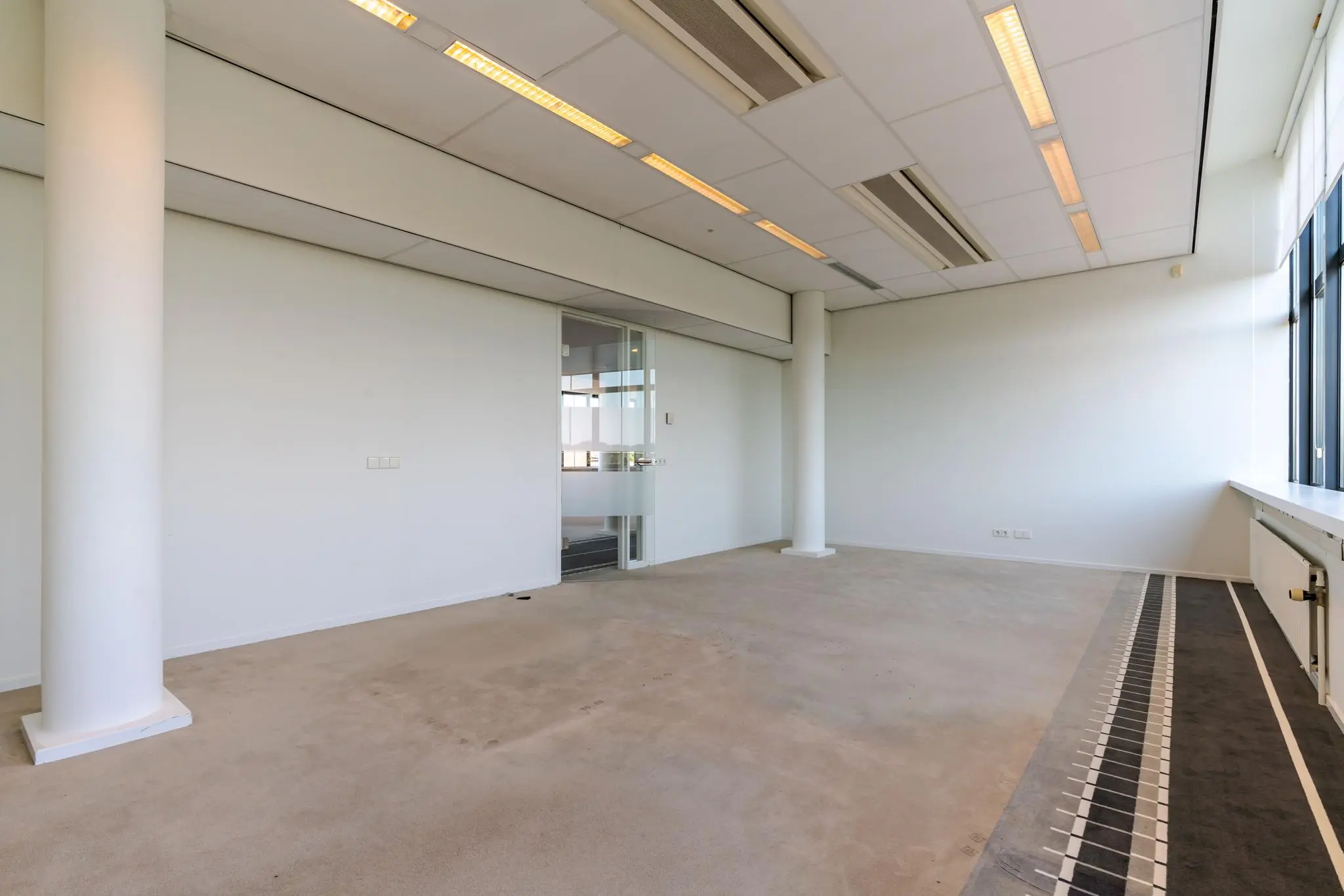 Leegstaand kantoorpand aan de Van Alkemadelaan met wit geschilderde muren, systeemplafond en grote ramen.